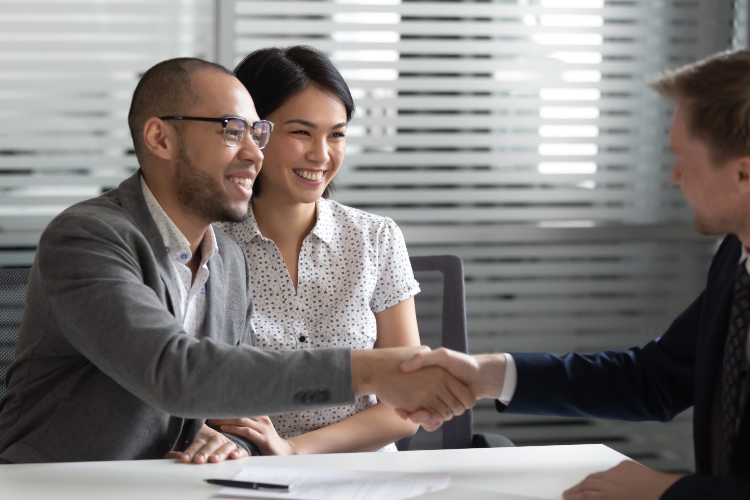 Cheerful mixed race married spouse shaking hands with financial advisor, lawyer, real estate agent, broker or bank manager after signing contract, buying insurance services, thanking for expert help.